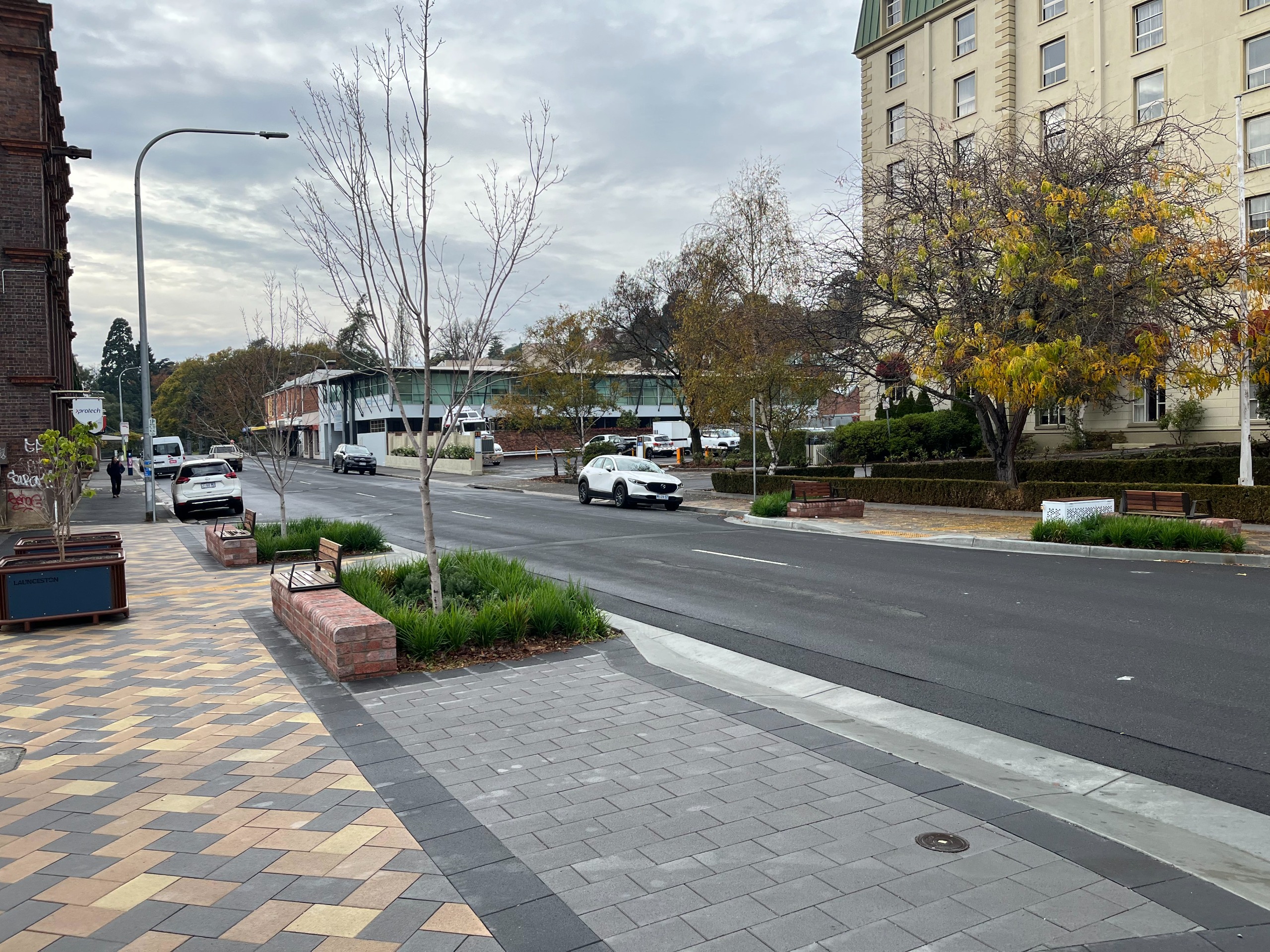A street crossing with trees, benches and greening.